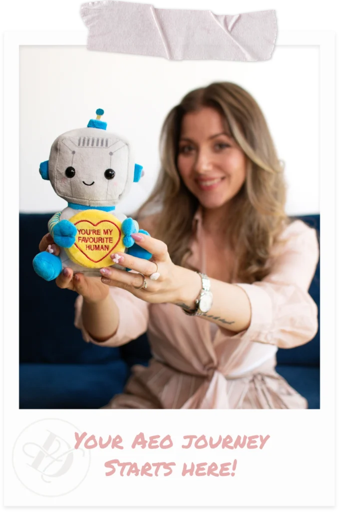 Blonde woman wearing pink blouse holding up robot plush toy